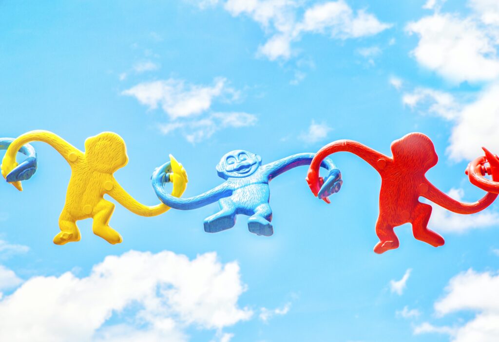 Plastic monkeys linked together in a chain against a blue, cloudy sky.